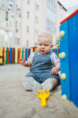 Fototapeta premium A 1-year-old child plays in the sandbox. A boy in summer clothes is playing on the street.