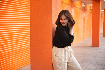 Woman Leaning Against Orange Wall With a Smile in an Urban Setting. smiling at the camera