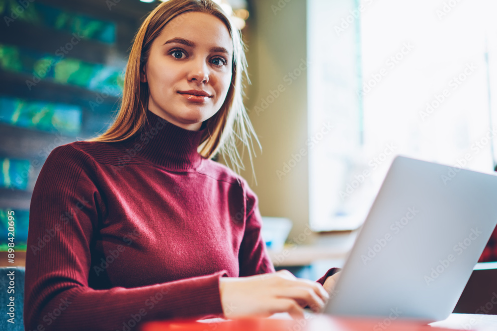 Poster portrait of skilled female student sitting in cafeteria with modern computer on table, caucasian hip