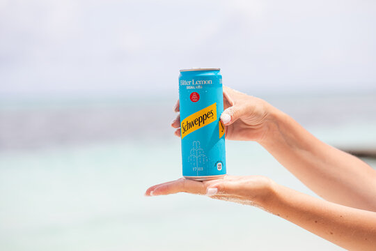 a steamed can of Schweppes in a woman's hand, ocean in the background
