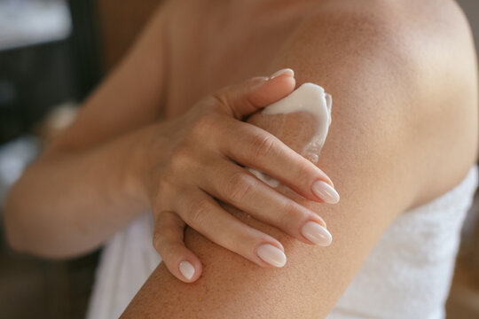 close up female hands and a smear of cream  or lotion or serum  on the skin, woman applies moisturizing cream or lotion after showering, daily body skin care routine 