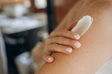 close up female hands and a smear of cream  or lotion or serum  on the skin, woman applies moisturizing cream or lotion after showering, daily body skin care routine 
