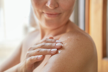  woman applies moisturizing cream or lotion after showering, daily body skin care routine 