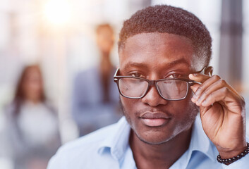 a black man in a blue shirt adjusts his glasses.
