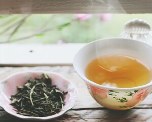 Sunlit Room Morning Serenity Close-Up of Steaming Green Tea in Porcelain Cup with Fresh Tea Leaves on Wooden Table
