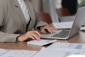 Business Woman Sitting at Desk Reviewing Work Documents on Laptop and Calculator in Modern Office Setting