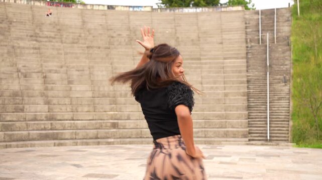 Full length of a latin young woman raising joining arms dancing salsa in a park