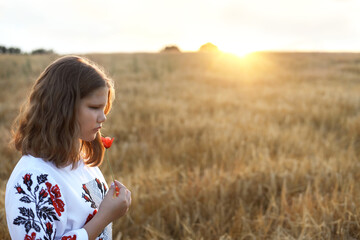 Sad girl wearing ukrainian vyshyvanka in the wheat field at the sunset holding poppies in her hands.A symbol of the blood of soldiers who died in the fight for the independence of Ukraine. Stop war