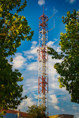 Mobile phone tower among vegetation and sky with clouds in the background.