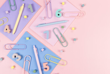 Top view of pink, purple and blue notebooks on pink background. Colorful pens, paperclips, numbers and pins. School, office wallpaper. Flat lay, copy space.