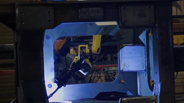 No people shot of yellow arm welding metal frame, producing blue sparks, computer-aided manufacture in tractor plant