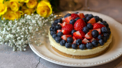 Cheesecake with berries close-up. Cake with strawberries and blueberries. Congratulations with flowers. Yellow roses on the table