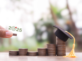 Close up of hand putting coins in stack of coins with graduation hat. The concept of saving money...