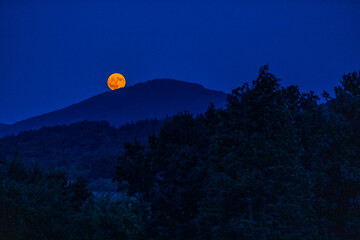 The full flower moon -  07, 2024. The rising moon over the mountain peaks , a cloudless night allows observation of the astronomical phenomenon. 