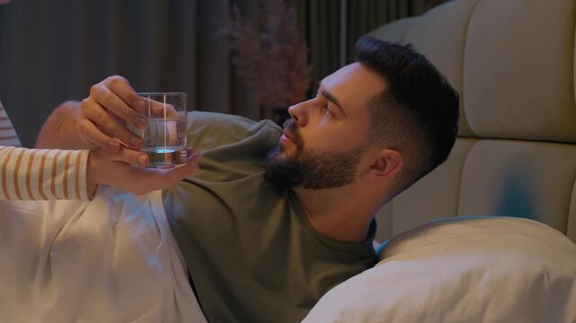 Man drinking water male sick husband woman wife female worried care helping love couple relationship illness unhealthy flu bed bedroom home treatment recovery suffering unwell grippe epidemic ailing