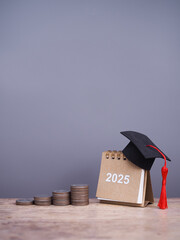 2025 Desk calendar with graduation hat and stack of coins. The concept of saving money for education, student loan, scholarship, tuition fees in year 2025