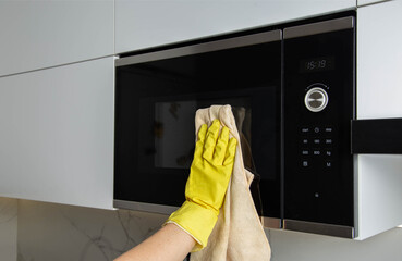 a dust cloth in the hand of a girl who wipes a microwave oven, the concept of cleaning the kitchen...