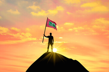 Waving flag of Maldives at the top of a mountain summit against sunset or sunrise. Maldives flag for Independence Day.