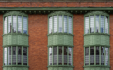 Red brick building with 3 green windows showcasing a symmetrical facade