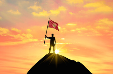 Waving flag of Montenegro at the top of a mountain summit against sunset or sunrise. Montenegro flag for Independence Day.
