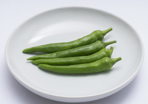 Close-up of four fresh green peppers on white dish, South Korea

