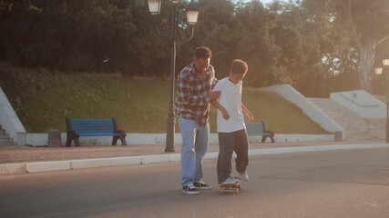 Man helping son standing on skateboard at empty road