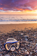 ocean cloudy morning landscape with diving mask on sea coast on foreground, sand of a beach, blue sea with surf and waves and cloudy sunset or sunrise on background