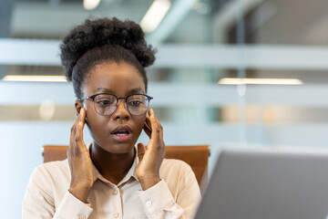 Worried female office worker receiving bad news at desk in modern workspace. Stressed professional...