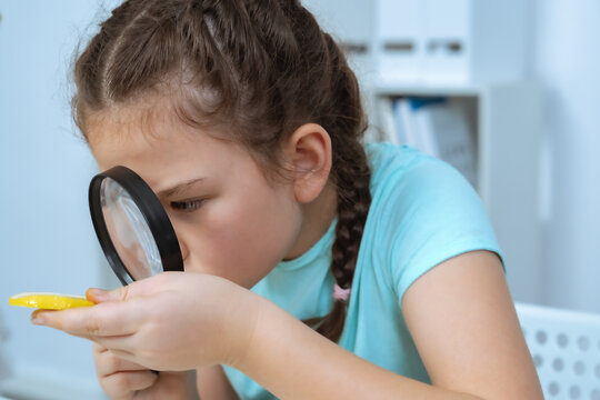 A young girl intensely examines a specimen using a magnifying glass, demonstrating her curiosity and interest in scientific exploration. Ideal for educational materials and promoting STEM learning.