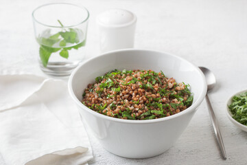 White bowl with boiled buckwheat and kale on a gray background, top view. Healthy homemade vegan food