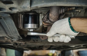 Close-up of auto mechanic using wrench to remove oil filter under car for car maintenance