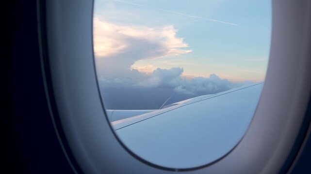 View Through Airplane Window Sunset Sky Fluffy Clouds Wing. Hand Held Camera Plane Warm Light Passenger POV.