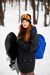 Young red hair woman snowboarder wearing protective goggles in front of winter forest