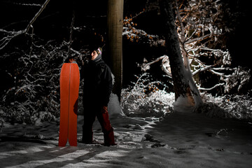 Man snowboarder dressed in dark sportswear and protective glasses standing with orange board...