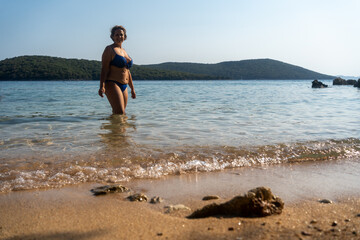 Portrait, bikini and happy plus size woman standing on beach for summer sunshine, vacation adventure and waves. Female person smile, swimwear and ocean for tropical holiday, relax in Greece