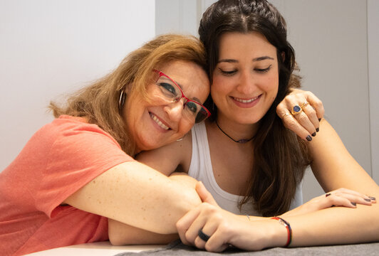 Attractive smiling older woman hugging her beautiful and happy young daughter sharing a precious family moment at home.