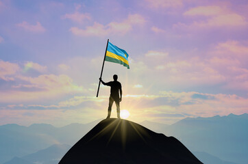 Waving flag of Rwanda at the top of a mountain summit against sunset or sunrise. Rwanda flag for Independence Day.