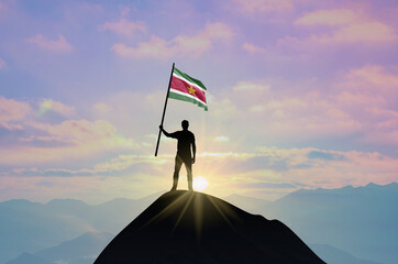 Waving flag of Suriname at the top of a mountain summit against sunset or sunrise. Suriname flag for Independence Day.