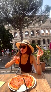 Girl in a hat eats pizza and drinks Aperol Spritz with the Colosseum background