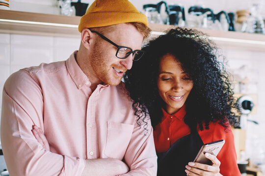 Positive african american female barista showing information on website on smartphone creative male manager with crossed hands collaborating with each other on developing own cafe business