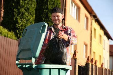 Man throwing trash bag full of garbage into bin outdoors, space for text