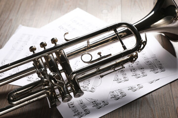 Obraz premium Trumpet and music sheet papers with notes on wooden table, closeup