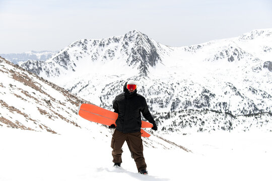 Young skier is standing and holding his red splitboard in his hands
