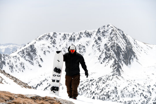 Young skier walks up the slope, holding his white splitboard in his hands