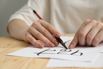 Calligraphy. Woman with brush writing word Reading in Hindi on paper at wooden table, closeup