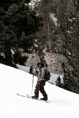 Young skier in ski goggles, hat and with backpack skis up the mountains