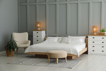 Stylish bedroom interior with comfortable bed, lamps, armchair and houseplants