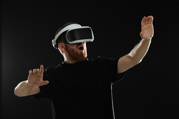 Emotional man using virtual reality headset on black background