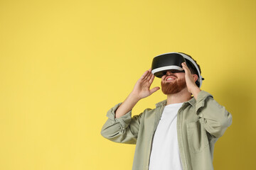Happy man using virtual reality headset on pale yellow background. Space for text