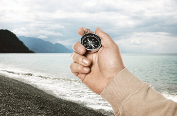 Man holding compass on beach near sea, closeup